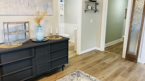 Un saló modern amb una consola de fusta fosca, un vas decoratiu i un quadre a la paret.