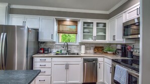 A modern kitchen with white cabinetry, stainless steel appliances, a dishwasher, and a window with blinds.
