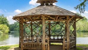 A wooden gazebo with a lattice roof, situated by a lake.