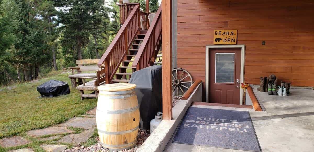 Een houten chalet met een houten trap die leidt naar een deur met daarop de tekst 'BEARS DEN'.