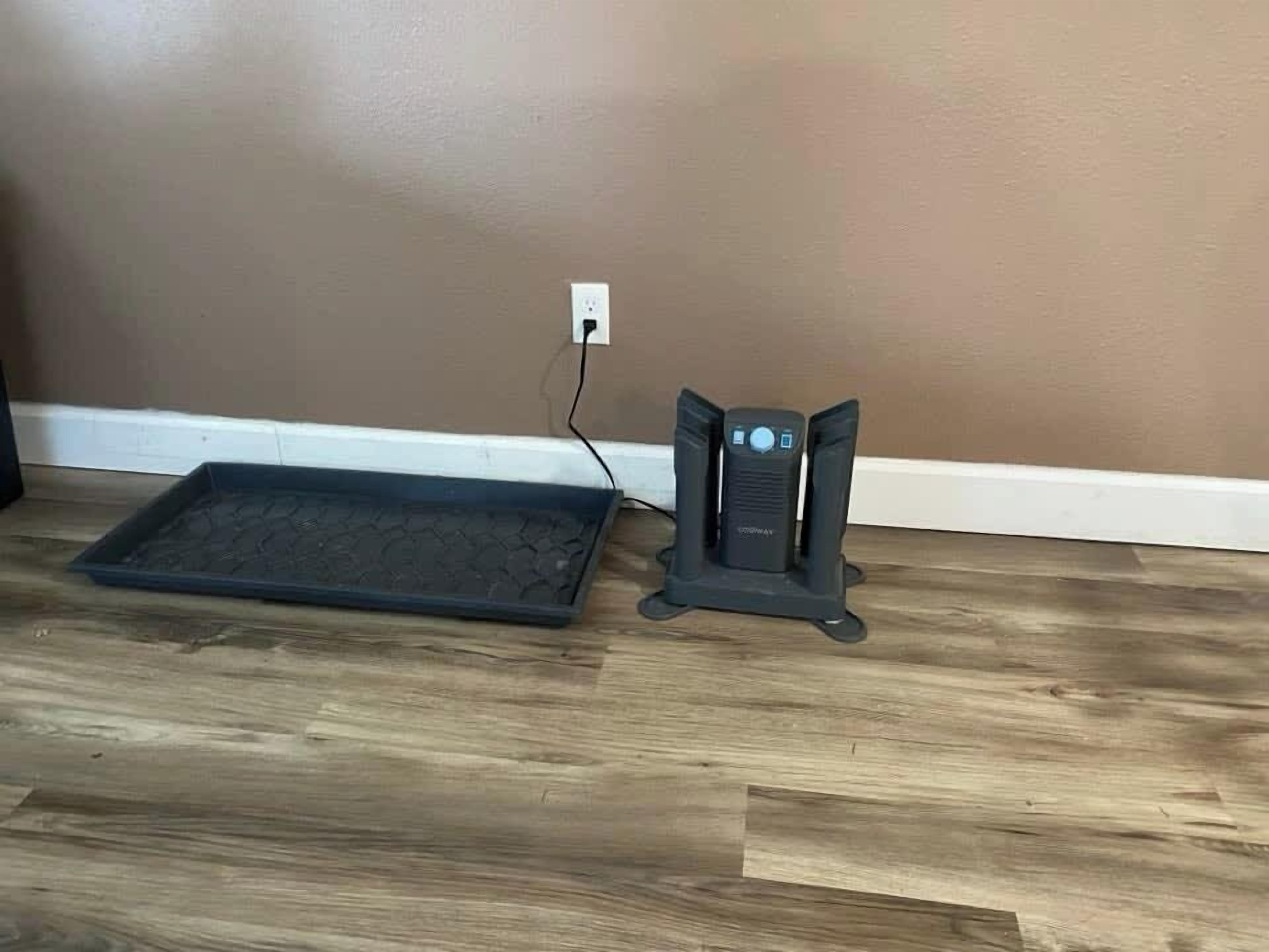 Calentador portátil negro sobre un piso de madera, cerca de un enchufe de pared.