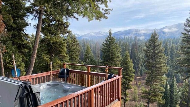 Ein Whirlpool auf einer Holzterrasse mit Blick auf einen Wald und Berge.