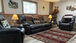 Ein Wohnzimmer mit einer Ledersofa, zwei Sesseln, einem gemusterten Teppich und Wanddekorationen, darunter Tier-Silhouetten und eine Bärenstatue.