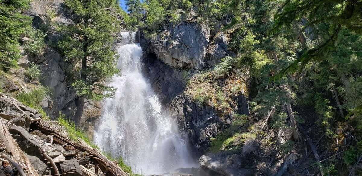 Ein Wasserfall, umgeben von dichtem Wald und felsigem Gelände.