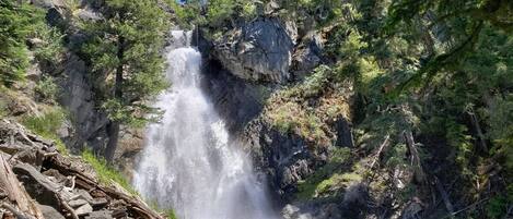 Ein Wasserfall, umgeben von dichtem Wald und felsigem Gelände.