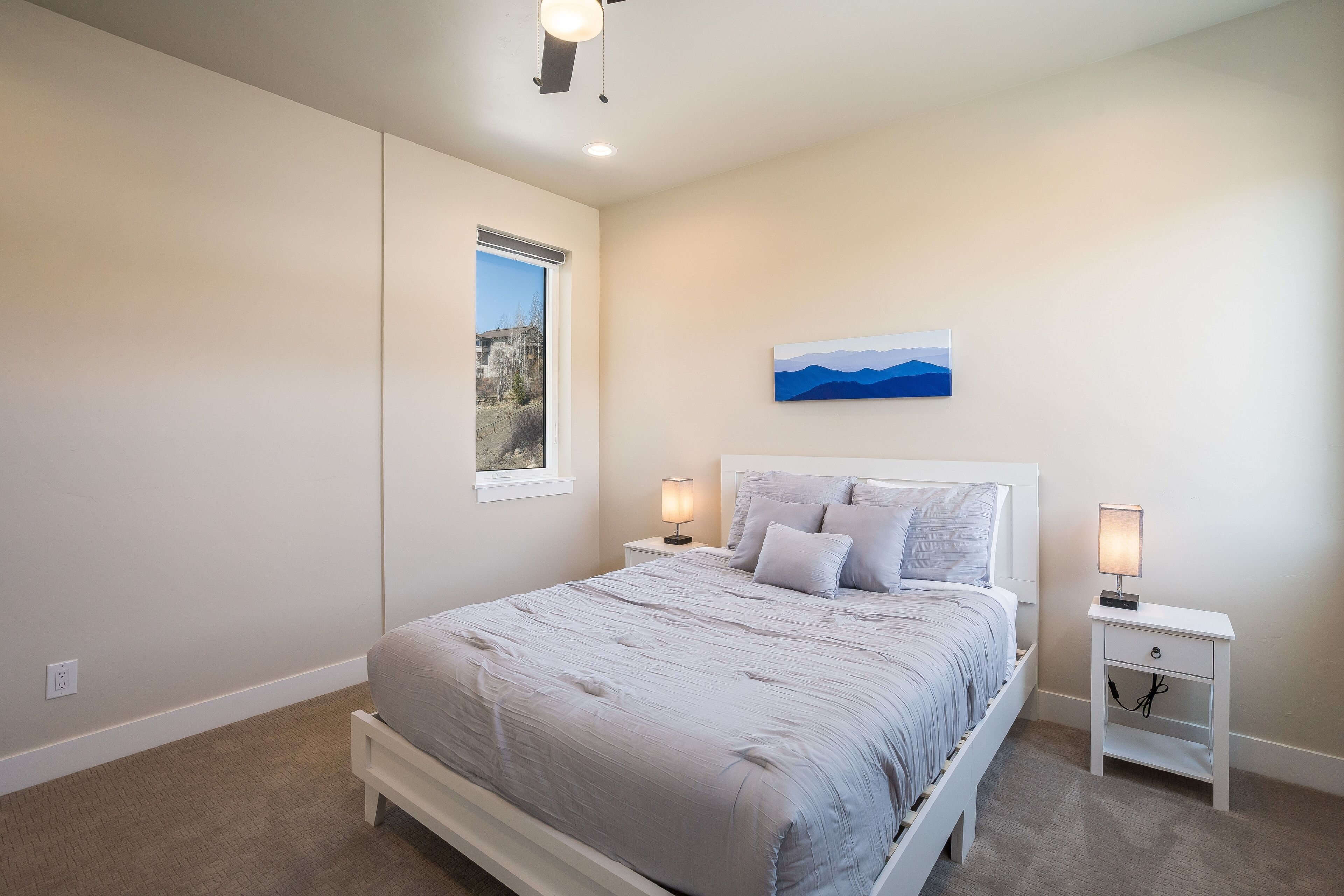 Une chambre à coucher comprenant un lit, deux tables de chevet, une fenêtre et un tableau accroché au mur.