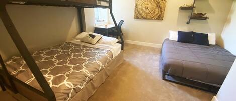 A room with two bunk beds, a desk, and a wall-mounted shelf.