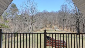 A wooden deck with a metal railing, a view of a forested area, and an American flag. - Knotty Knob is your mountain get away! (Frametown)