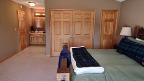 A bedroom with a bed, a nightstand, a lamp, and two doors leading to a bathroom and a kitchen. - Knotty Knob is your mountain get away! (Frametown)