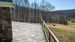 A wooden deck with a stone wall on one side, leading to a grassy area with trees in the background. - Knotty Knob is your mountain get away! (Frametown)
