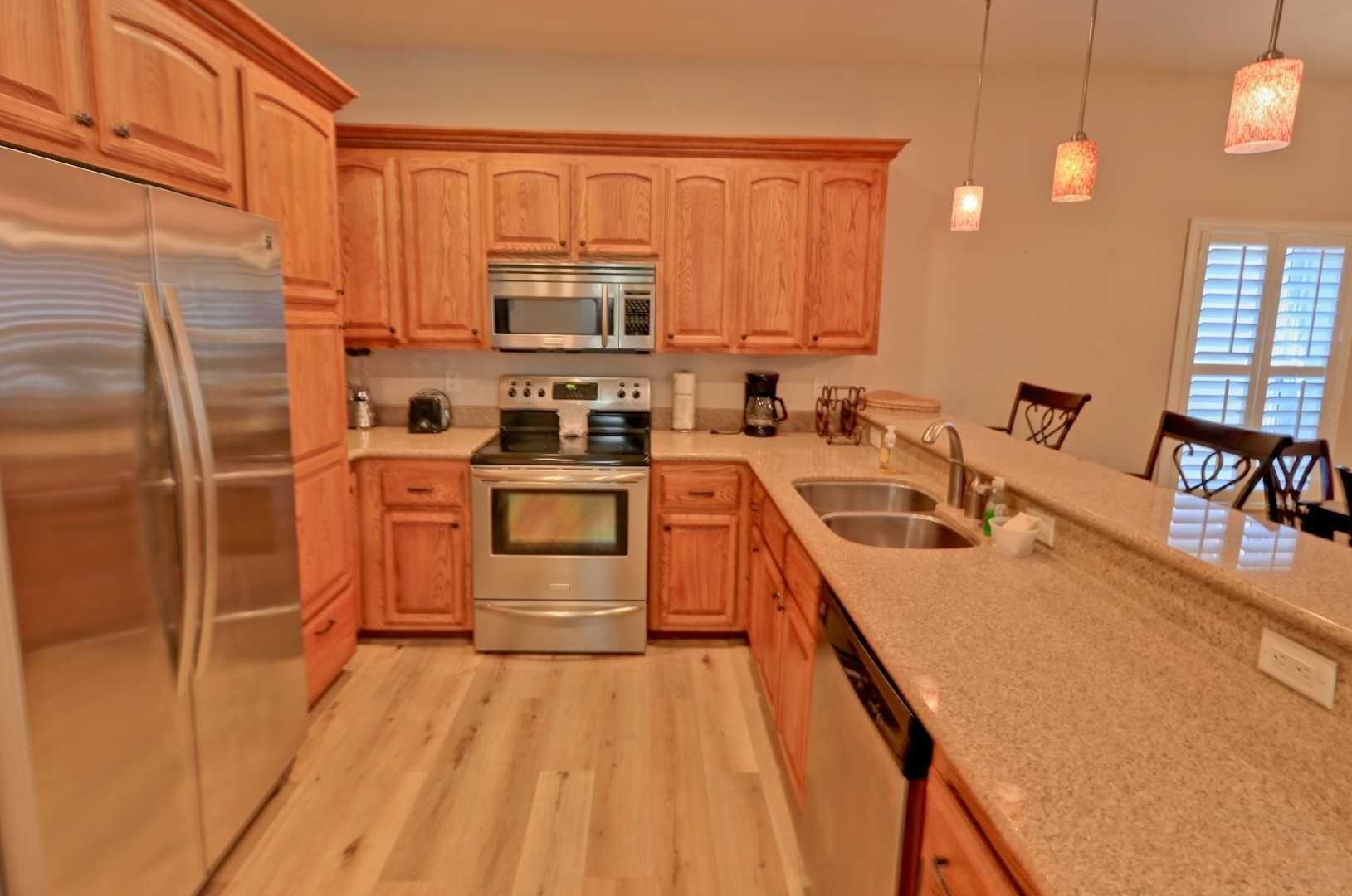 A modern kitchen with wooden cabinets, stainless steel appliances, granite countertops, and pendant lighting.