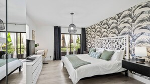 Un dormitorio moderno con una cama grande, un televisor, un escritorio y vistas a zonas verdes.