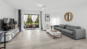 Una sala de estar moderna con un sofá gris, una mesa de centro, un televisor y un balcón con zona de comedor.