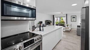Una cocina moderna con electrodomésticos de acero inoxidable, una isla grande y vistas a un área de estar con sofá y televisor.