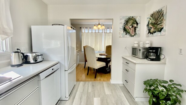 Une cuisine moderne avec des appareils électroménagers blancs, un coin repas avec une table et des chaises en bois, et un petit espace dédié à la préparation du café.