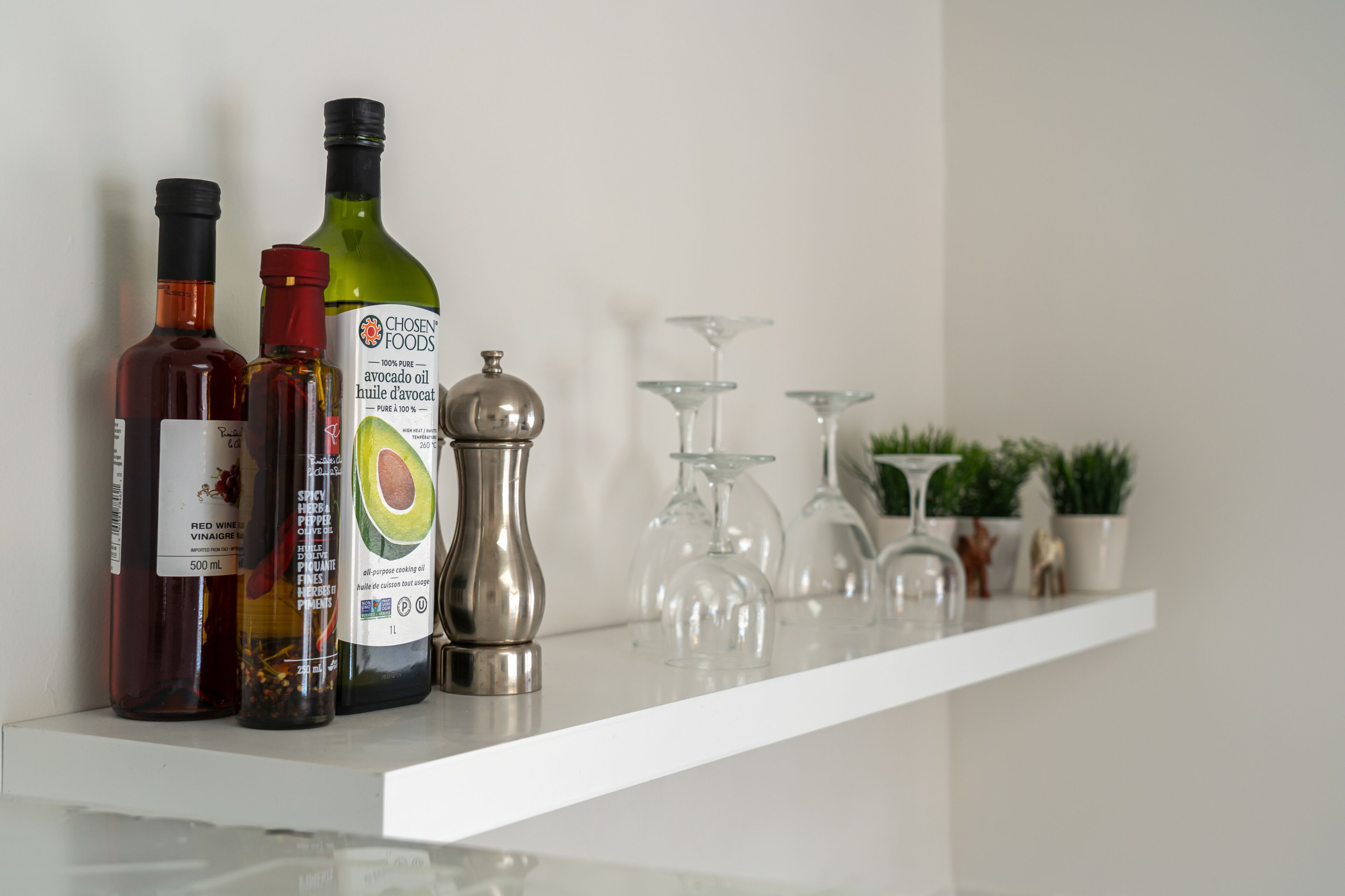 A kitchen shelf with various bottles of cooking oils and a pepper grinder.