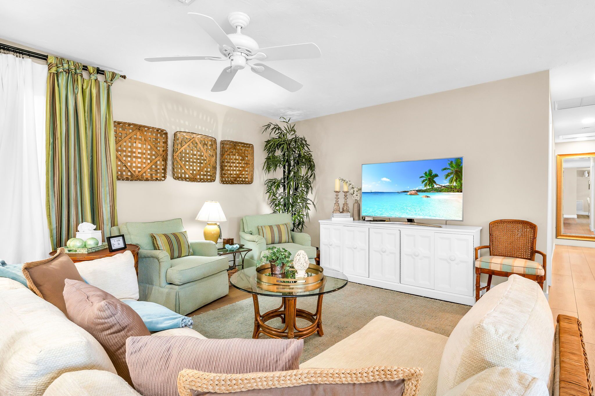 A living room with a green sofa, a glass coffee table, and a television displaying a beach scene.
