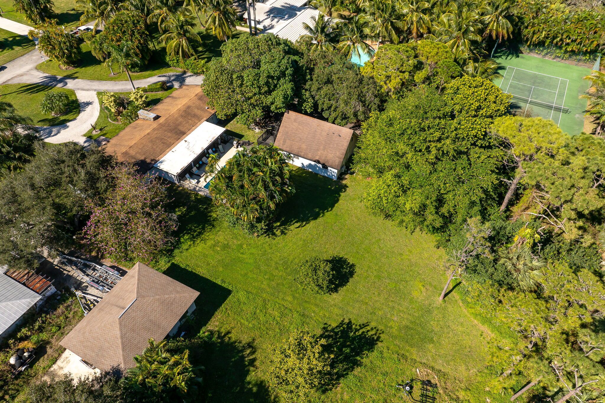 Vista aérea de una zona residencial con dos casas, una cancha de tenis y vegetación circundante.