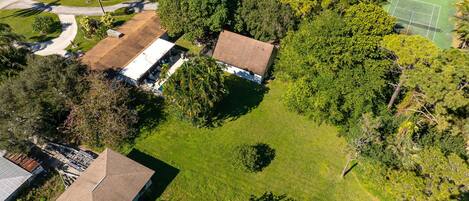 Vista aérea de una zona residencial con dos casas, una cancha de tenis y vegetación circundante.