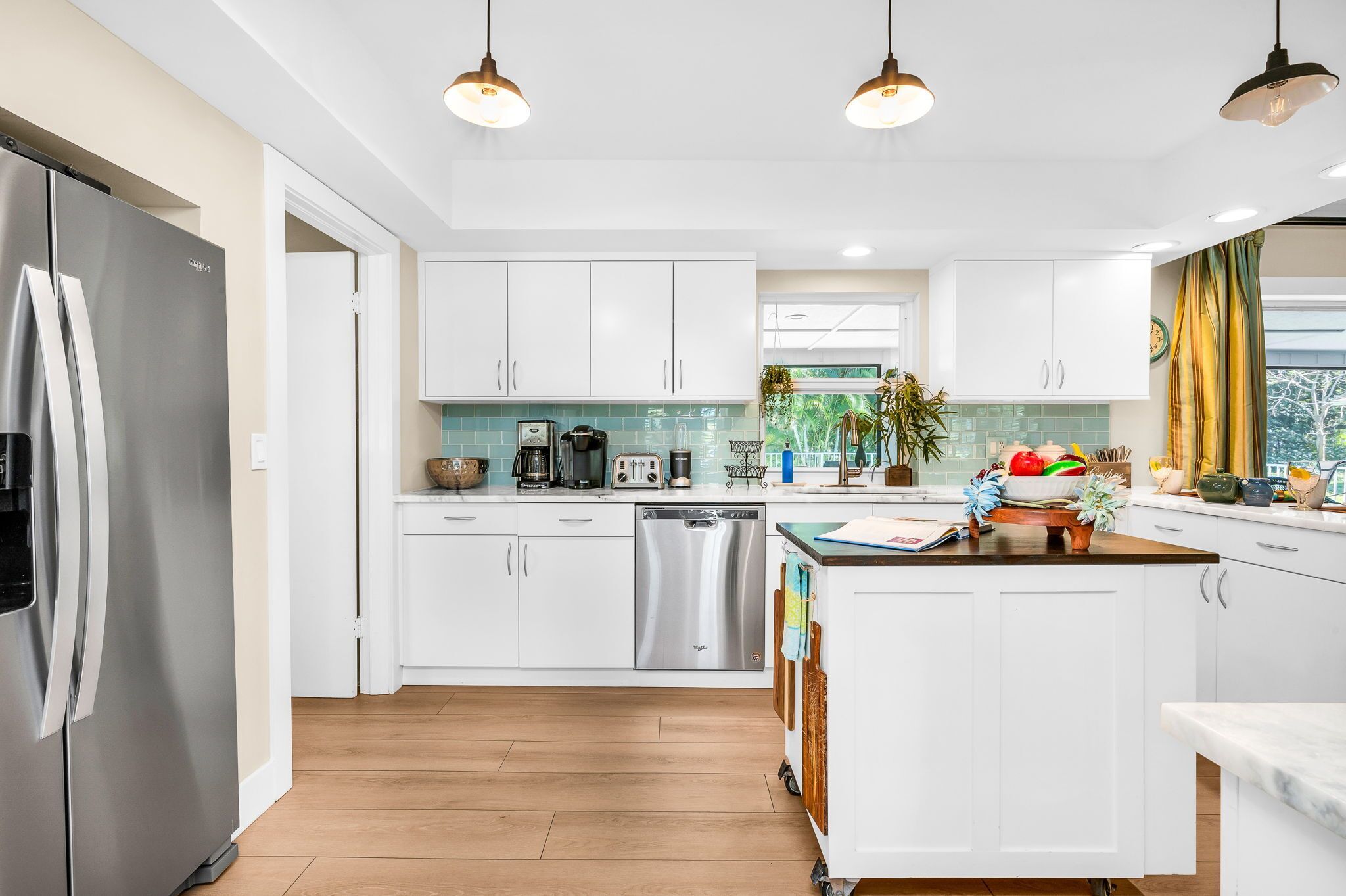 A modern kitchen with white cabinets, stainless steel appliances, and pendant lighting.