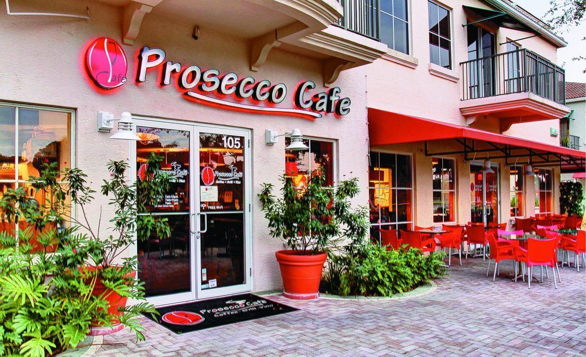 Ein Café mit Außenbereich, einer großen Topfpflanze und einem Neonzeichen.