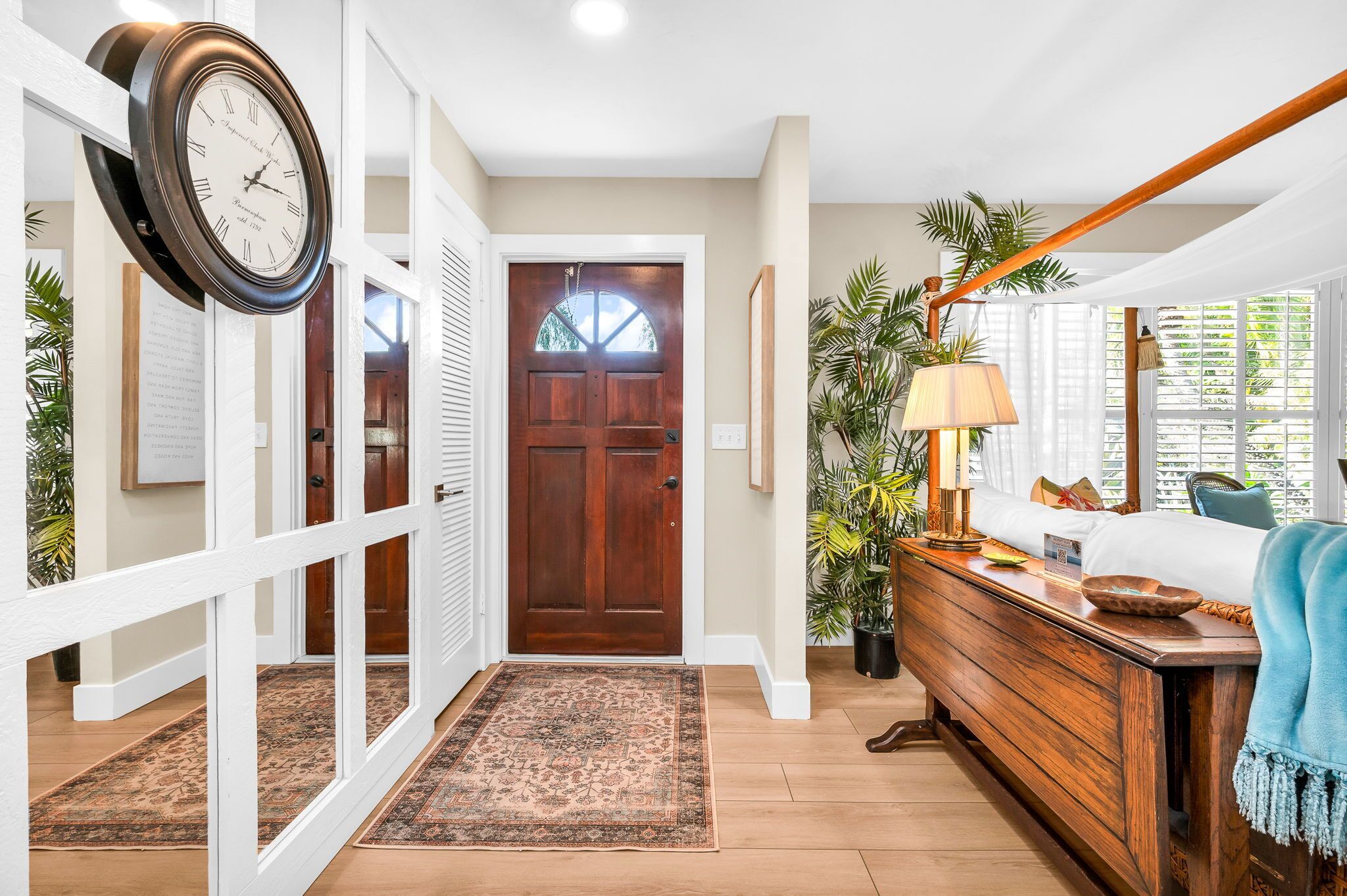 A hallway with a wooden door, a clock, a lamp, and a bench with a blue throw.