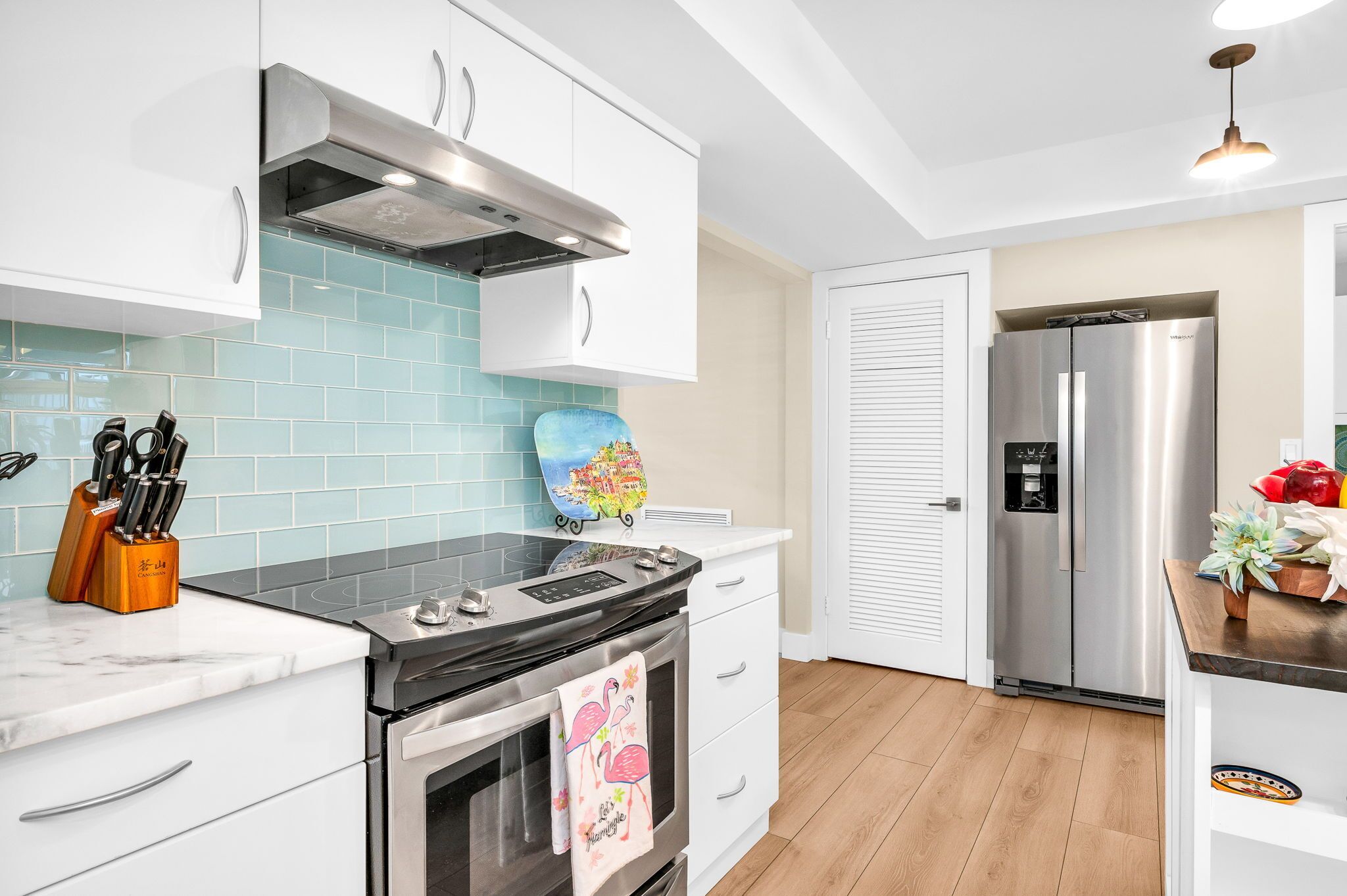 Una cocina moderna con armarios blancos, un refrigerador de acero inoxidable y un salpicadero de azulejos.