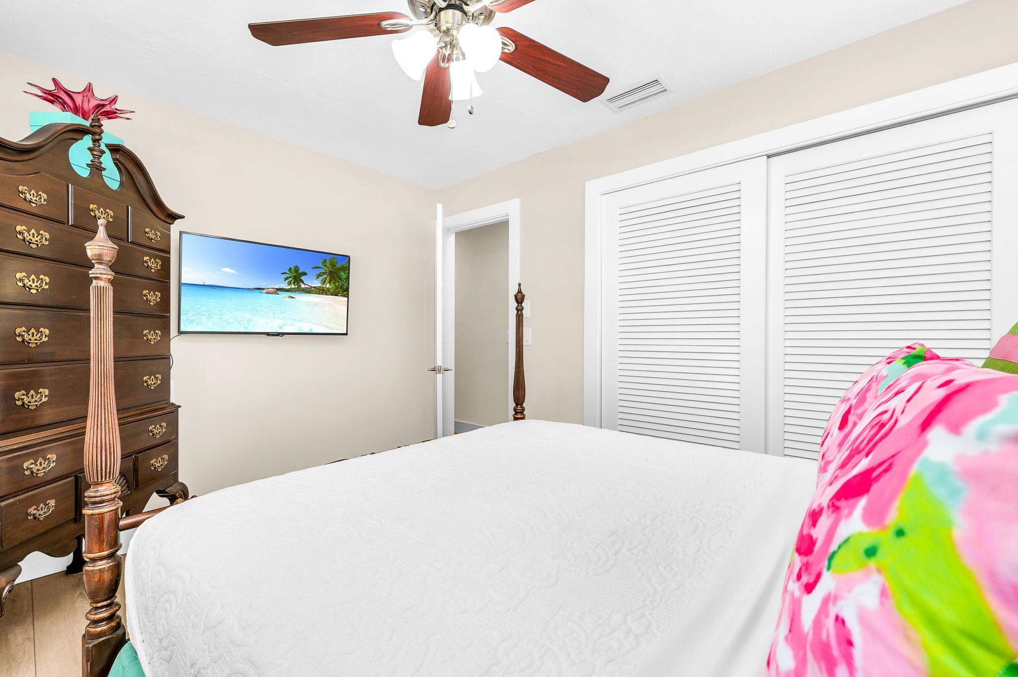A bedroom with a bed, a dresser, a ceiling fan, a television, and a closet.