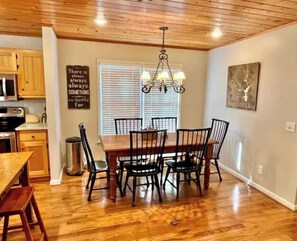 A dining area with a wooden table and chairs, a chandelier, a kitchen with wooden cabinets, and a wall with a motivational quote. - Amazing Lake  / Mountain Setting (Westminster)
