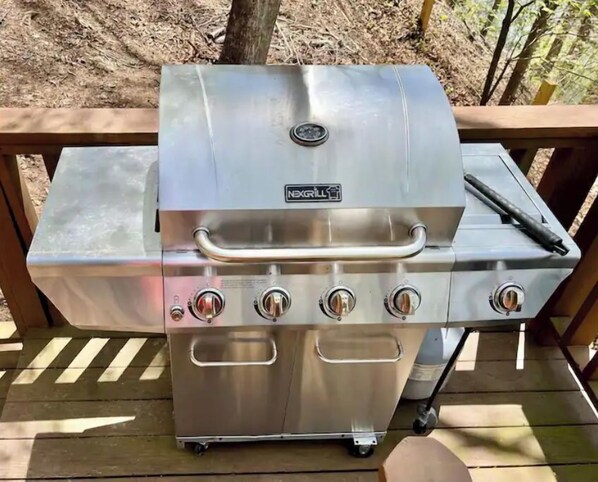 Un barbecue portable en acier inoxydable, doté de quatre brûleurs, d ’une poignée et d’une tablette latérale, placé sur une terrasse en bois.