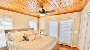 Ein Schlafzimmer mit Holzbalkendecke, einem Bett mit beigefarbener Bettwäsche, einem Deckenventilator und weißen Fensterläden.