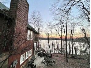 Situated by the water, this cabin features a deck with outdoor seating and a brick chimney.