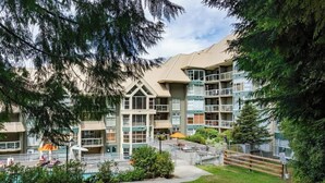 A multi-story residential building with balconies, a swimming pool, and a fenced patio area. - Upper level condo w/ AC & hot tub (Whistler)