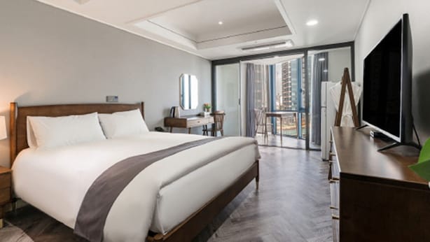 Habitación de hotel moderna con una cama grande, un escritorio, televisión y un balcón con vistas a edificios.