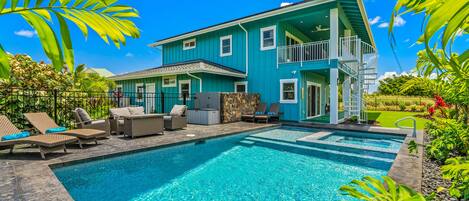 A two-story house with a swimming pool, outdoor furniture, and tropical plants.