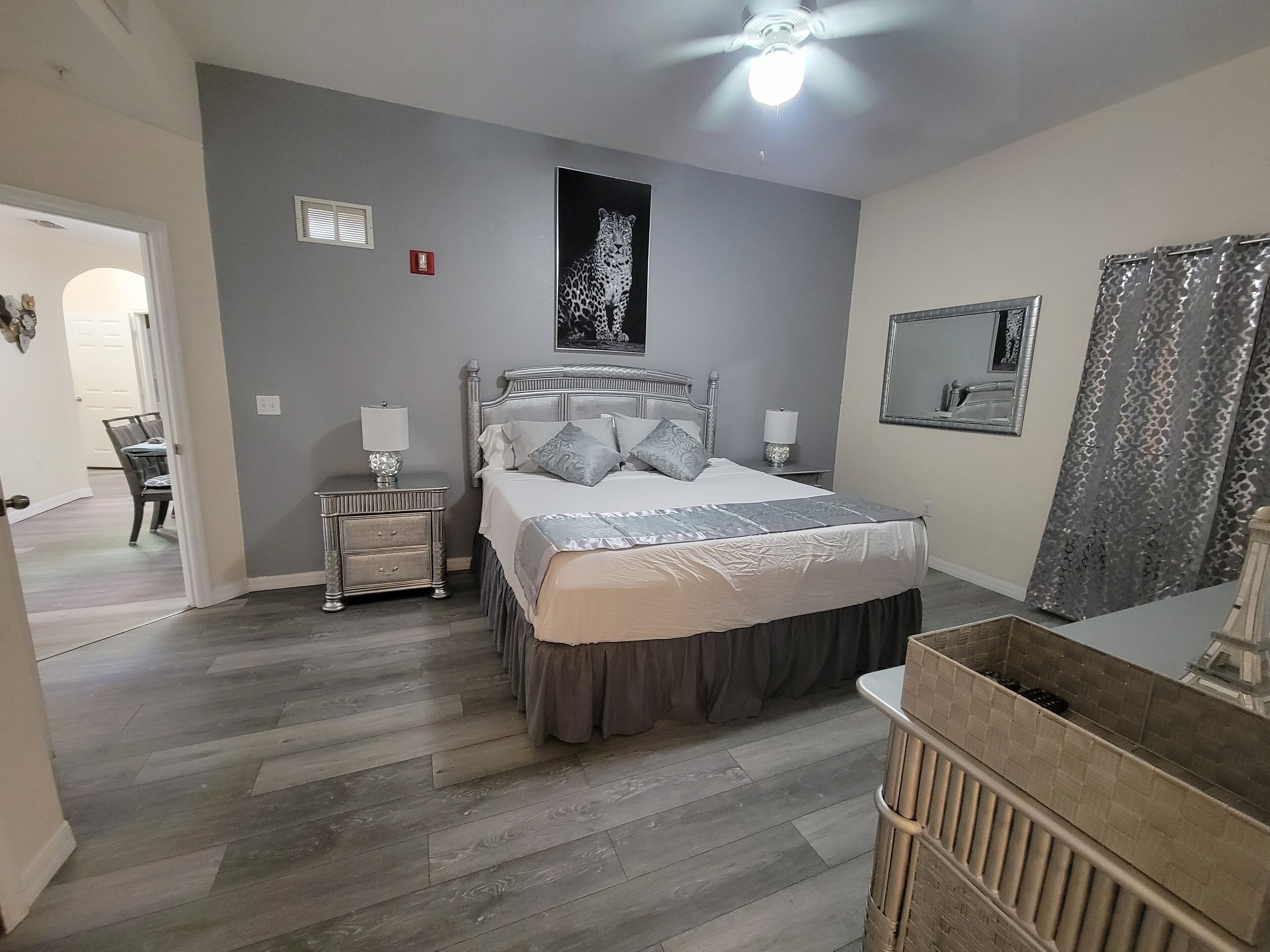A bedroom with a bed, nightstands, a ceiling fan, a mirror, and a door leading to another room.