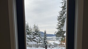 En dør, der fører til et sneklædt udendørsområde med en bænk og en bil i nærheden.