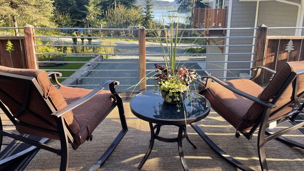 En terrasse med to brune stole og et bord, med udsigt over en sø og skov.