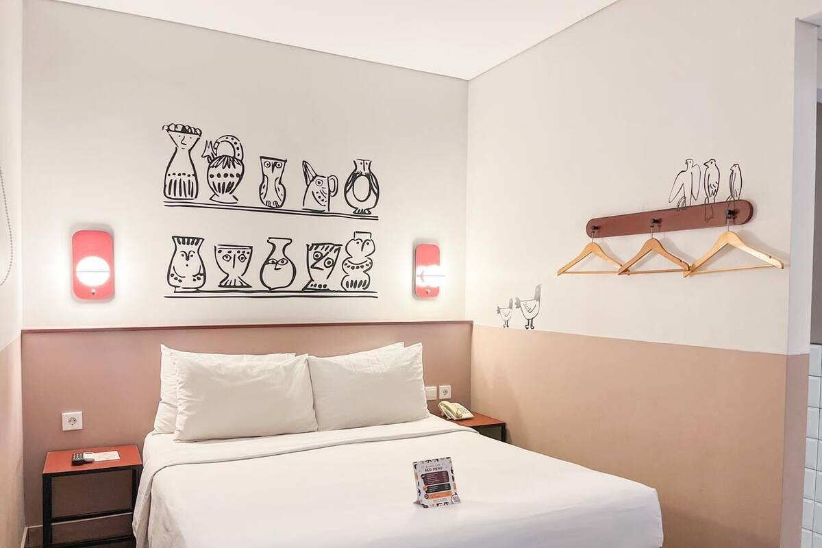 Ein Hotelzimmer mit Bett, Nachttischen, einem an der Wand befestigten Kleiderhaken und einem dekorativen Wandbild.