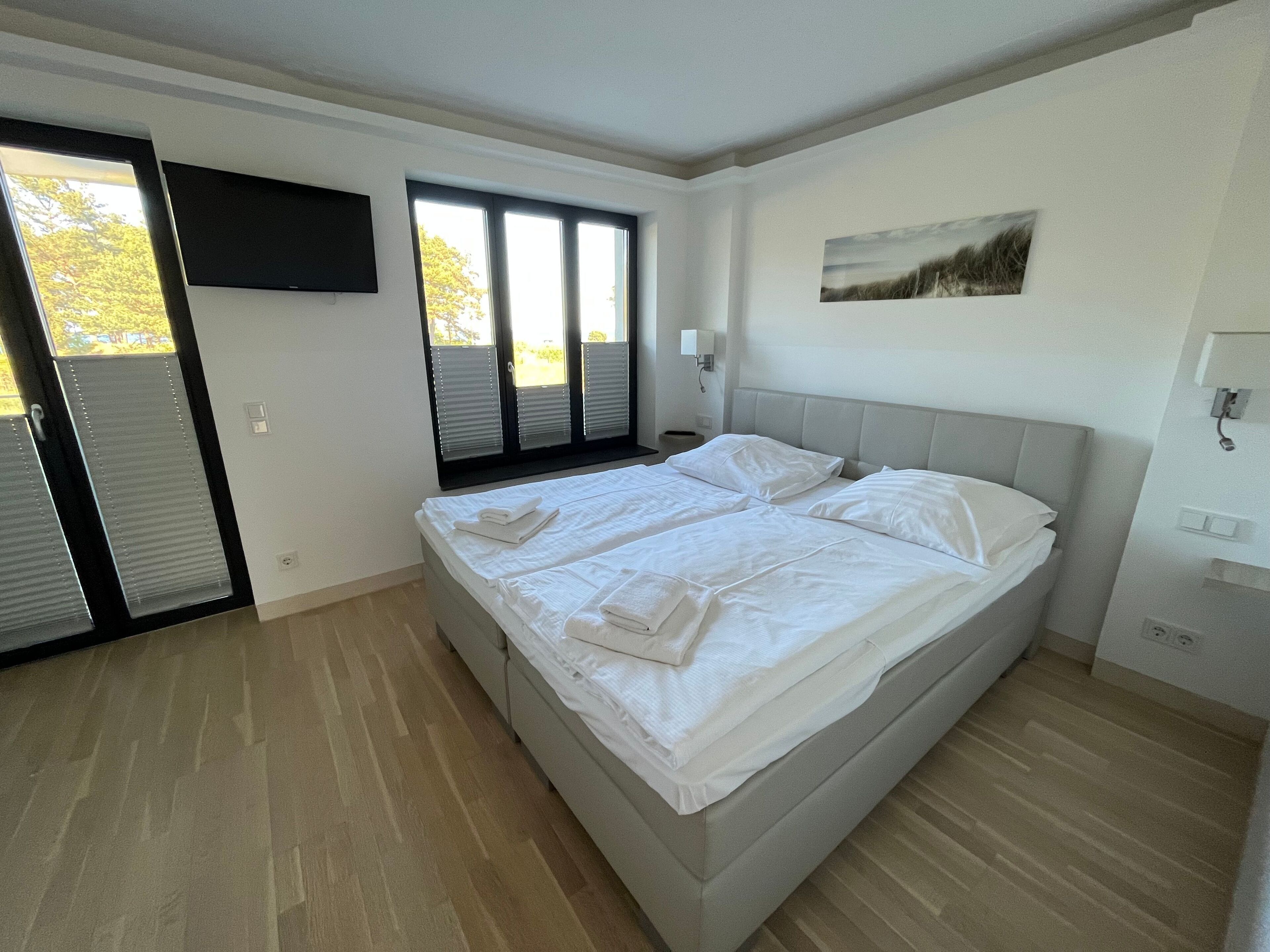 Een slaapkamer met een groot bed, een aan de muur bevestigde televisie en een raam met jaloezieën.