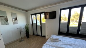 A bedroom with a bed, a potted plant, a TV, and a sliding door to a balcony.