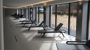 A modern hotel lobby with rows of sun loungers, large windows, and a minimalist design.
