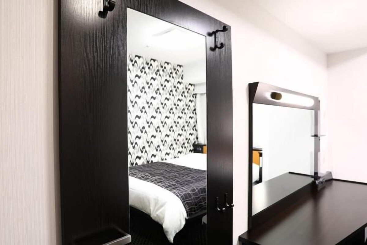 A hotel room with a bed, a desk, a mirror, and a wall with a patterned wallpaper.
