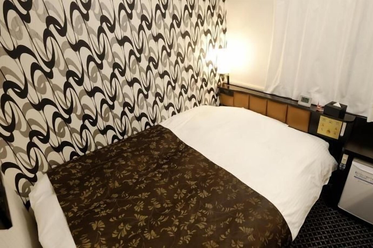 A hotel room with a bed, a nightstand, a coffee maker, and a small refrigerator.