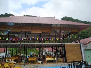 A covered outdoor seating area with tables and chairs, a wooden structure, and colorful flags. - Occult Lan Ha Farmstay Mt (Hai Phong)