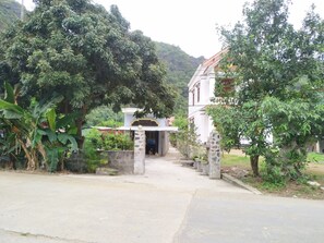 A building with a stone entrance, surrounded by lush greenery and a paved pathway leading to it. - Occult Lan Ha Farmstay Mt (Hai Phong)