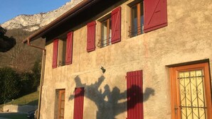Un edificio con contraventanas rojas, una puerta de madera con reja de metal y una sombra proyectada en la pared.