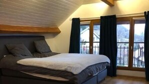 Un dormitorio con una cama grande, suelo de madera, techo inclinado y un balcón con cortinas.