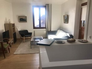 Una sala de estar con un sofá, una mesa de centro, un televisor y una estantería.