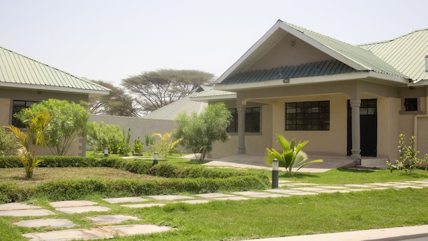 A modern building with a symmetrical design, featuring a central entrance with a covered porch, surrounded by well-maintained lawns and pathways. - Cairo Palace Hotel (Lodwar)